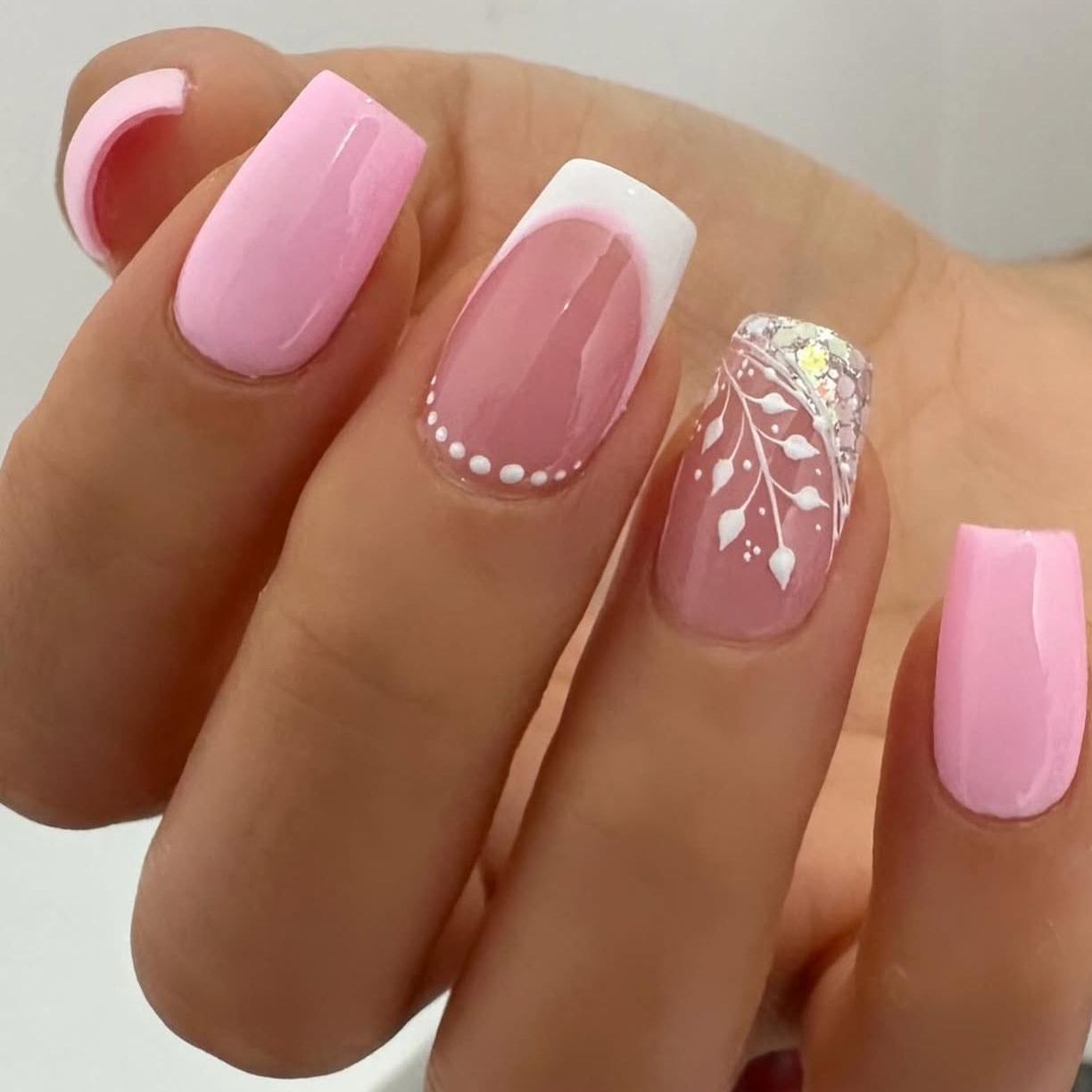 Uñas rosa chicle con francesa blanca, puntitos y hojas pintadas a mano con brillo