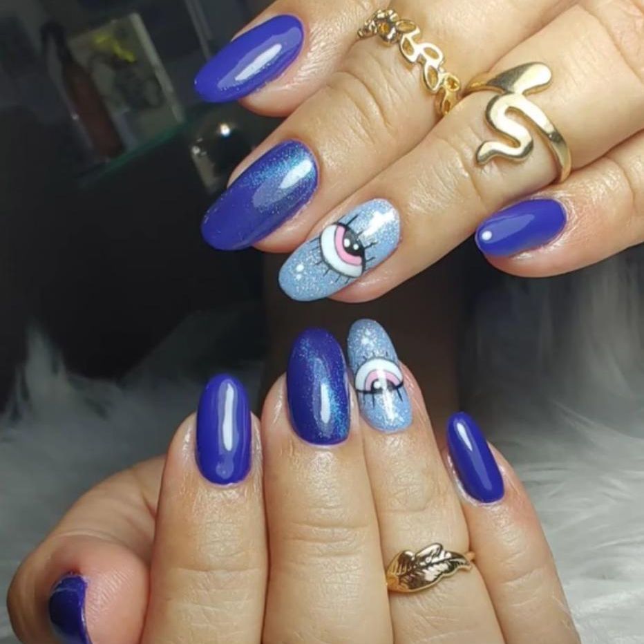 Uñas azul cobalto con dos diseños en celeste: un ojo y un arcoíris